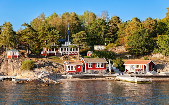 Red cottages on a rocky shore surrounded by trees in the Stockholm archipelago.