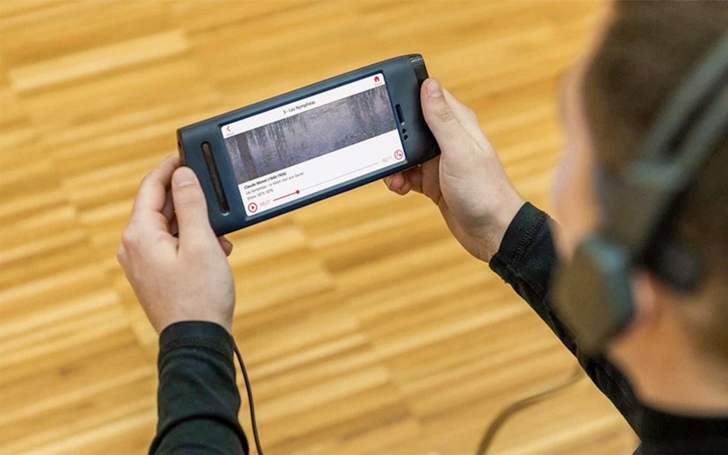 Visitor using audio guide at Orangerie Museum, Paris, viewing Claude Monet's artwork.