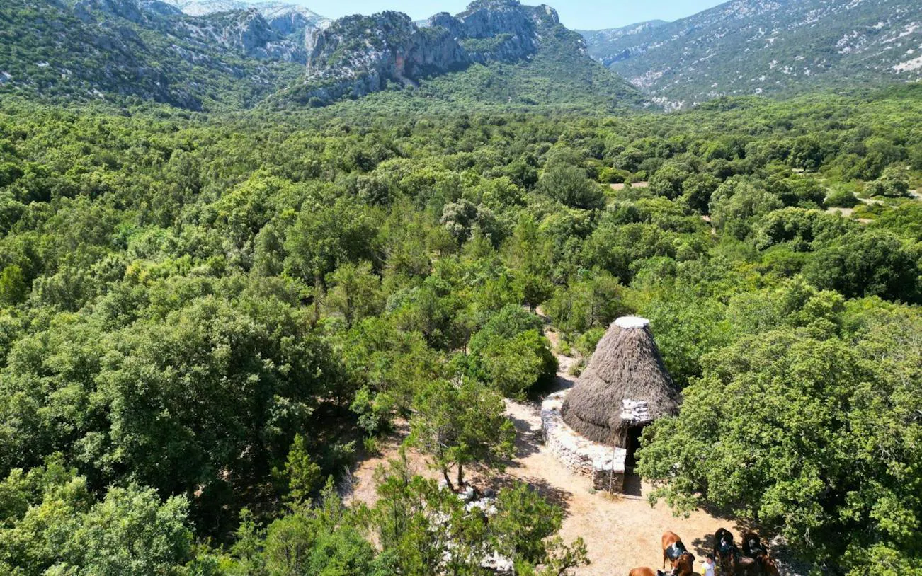 Horseback riders near traditional hut in Lanaitto Valley, Oliena, surrounded by lush greenery and mountains.