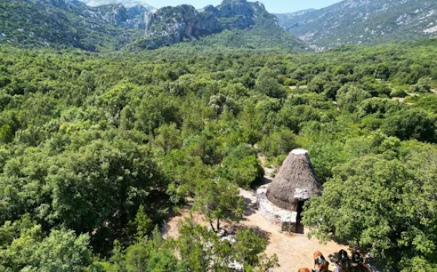 Horseback riders near traditional hut in Lanaitto Valley, Oliena, surrounded by lush greenery and mountains.