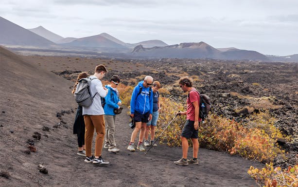 Group trekking in Timanfaya Volcano Natural Park, Lanzarote, with volcanic landscape.
