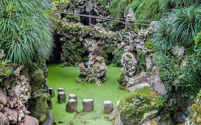 Stepping stones over green water at Waterfall Lake, Quinta da Regaleira, Sintra, Portugal.