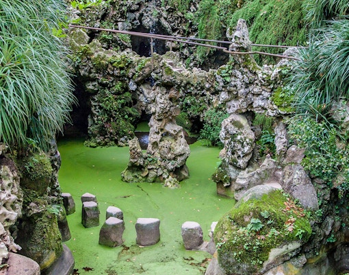 Waterfall cascading into a serene lake at Quinta da Regaleira, Sintra, Portugal.