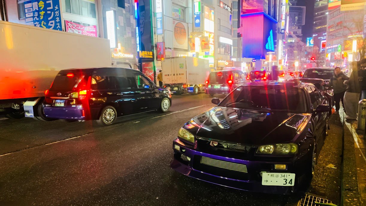 Supercar parked on a busy street in Tokyo at night, surrounded by vibrant city lights.