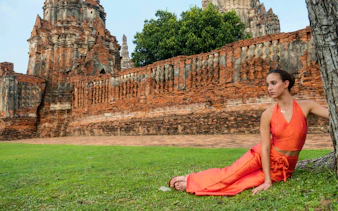 Ancient brick temple ruins in Ayutthaya, Thailand, with a person sitting nearby.