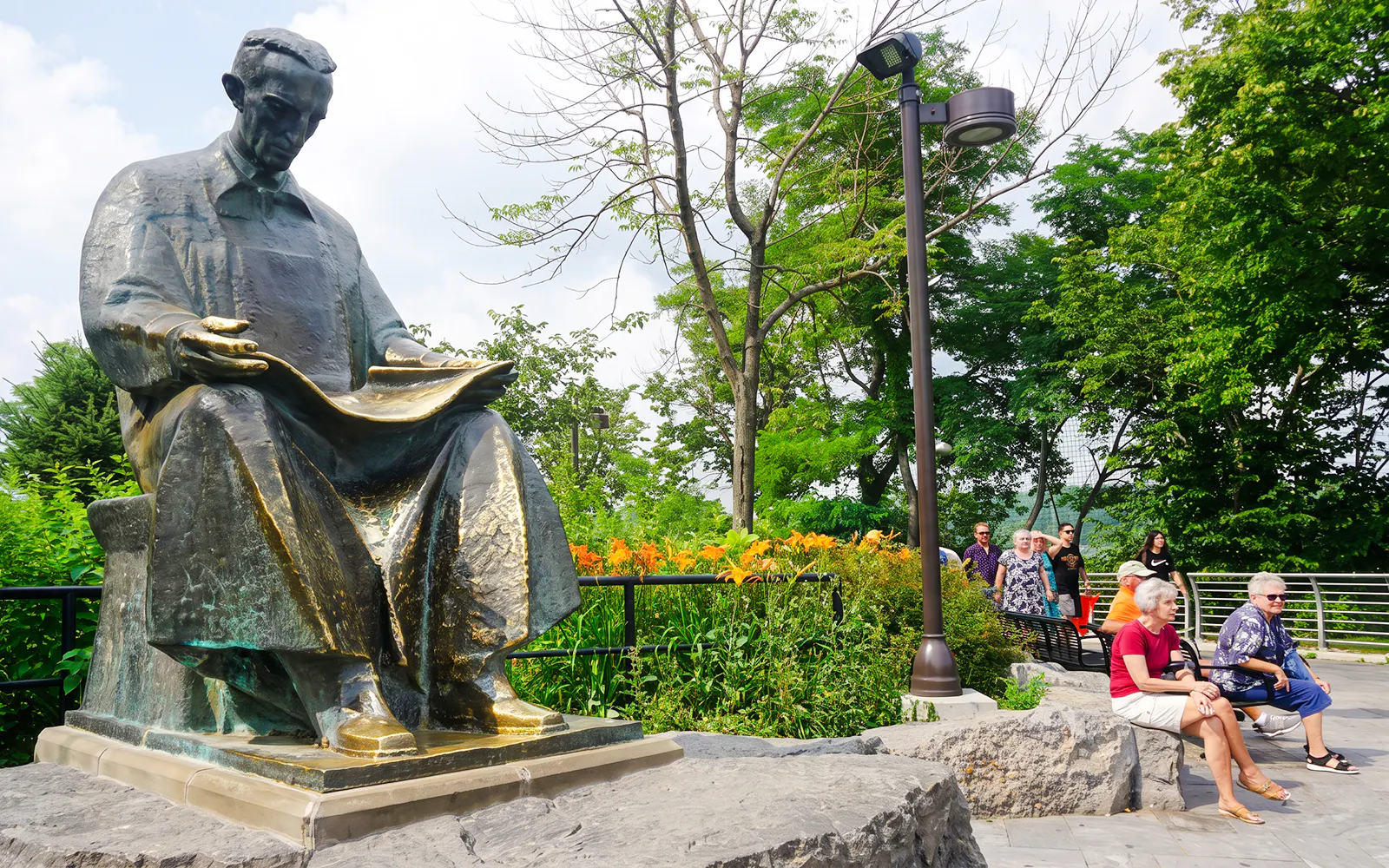 Statue of Nikola Tesla in a park setting with tourists nearby, Niagara Falls walking tour.
