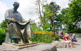 Statue of Nikola Tesla in a park setting with tourists nearby, Niagara Falls walking tour.