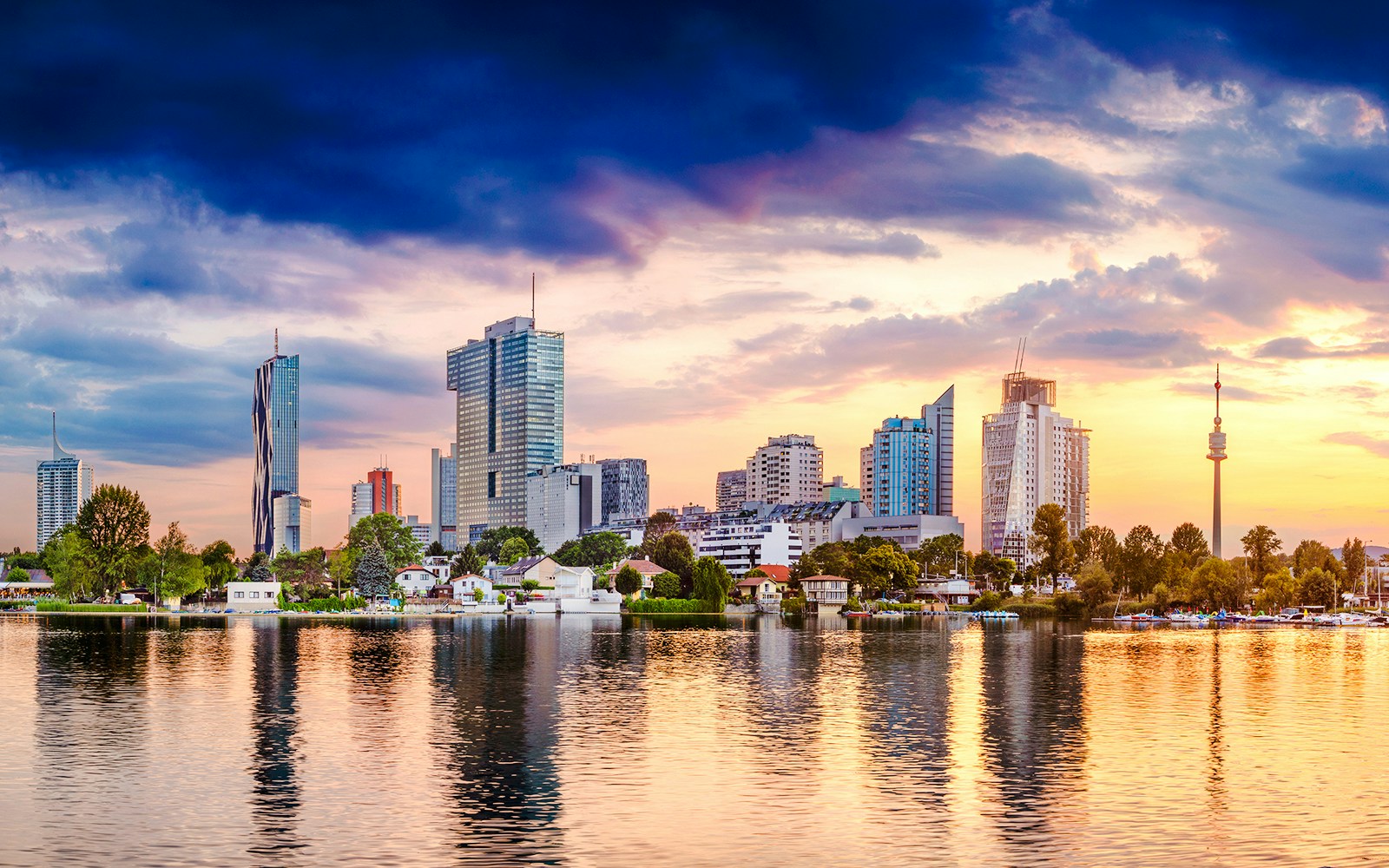 Panoramic view of Vienna skyline with modern buildings and Danube River at sunset.