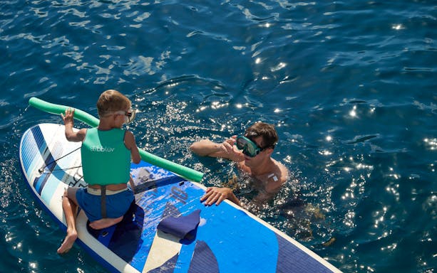 Child on paddleboard with adult in water during Catamaran Cruise near Spinalonga, Crete.