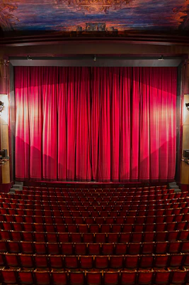 Interior of a London theatre with red seats and closed stage curtain.