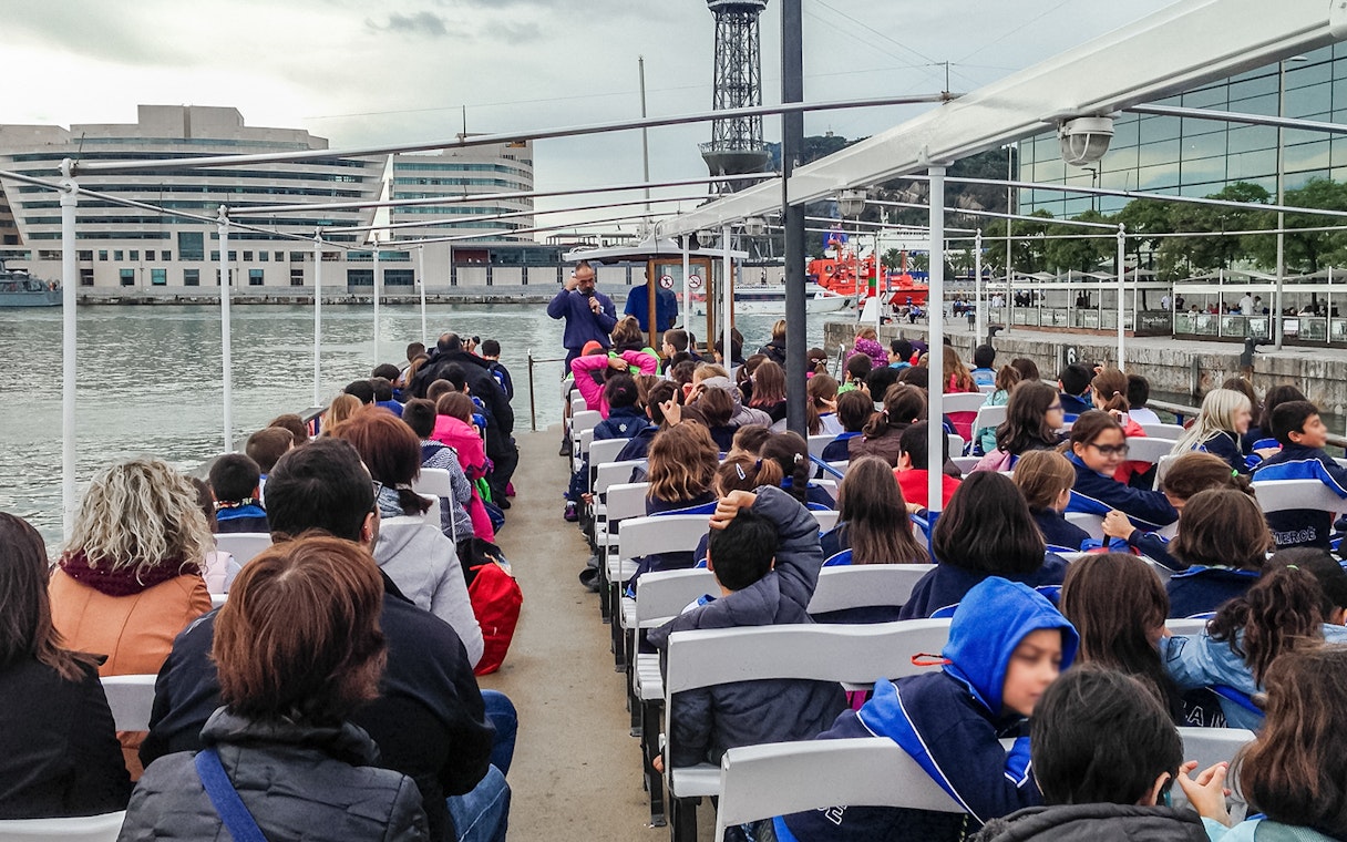 Passengers seated on Las Golondrinas boat trip in Barcelona, viewing cityscape and waterfront.