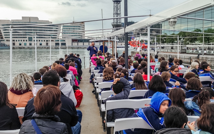 Passengers seated on Las Golondrinas boat trip in Barcelona, viewing cityscape and waterfront.