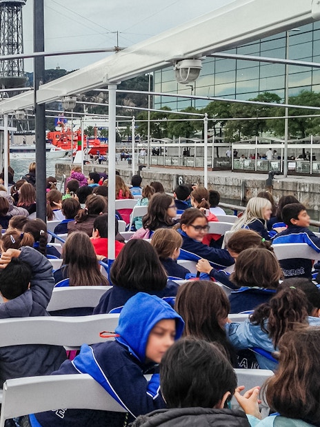 Passengers seated on Las Golondrinas boat trip in Barcelona, viewing cityscape and waterfront.