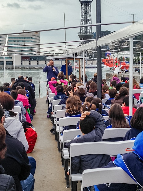 Passengers seated on Las Golondrinas boat trip in Barcelona, viewing cityscape and waterfront.