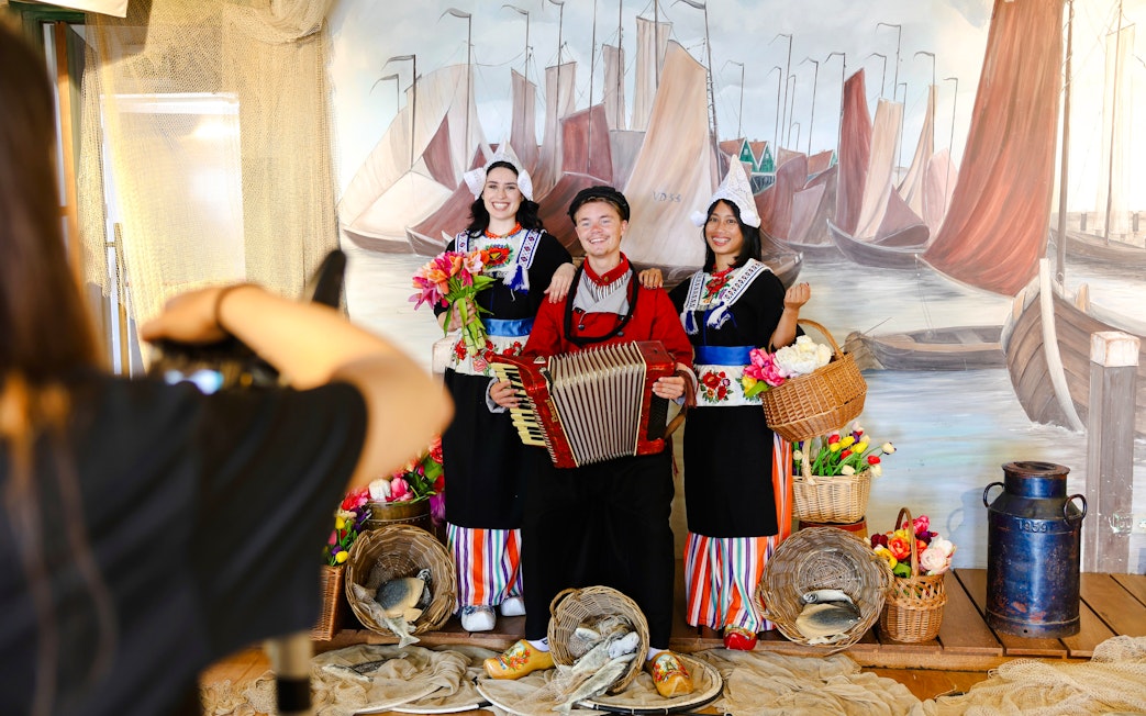 Tourists in traditional Volendam costumes posing with an accordion and baskets of flowers.