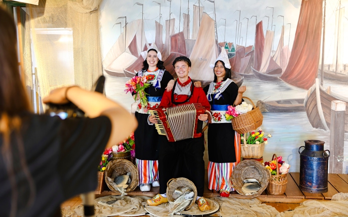 Tourists in traditional Volendam costumes posing with an accordion and baskets of flowers.