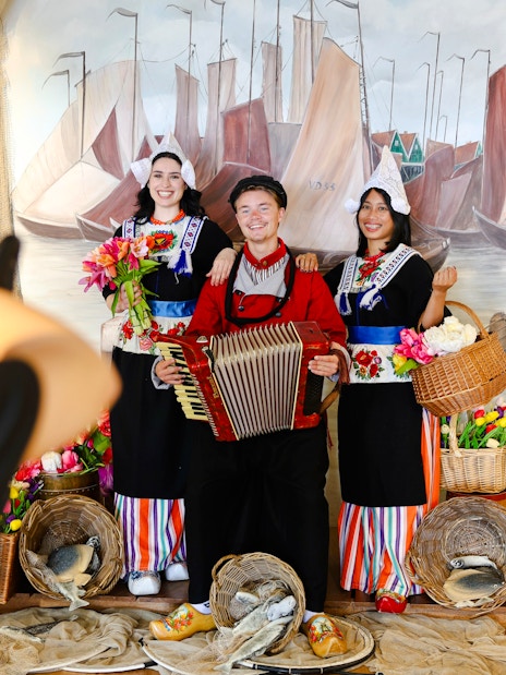 Tourists in traditional Volendam costumes posing with an accordion and baskets of flowers.