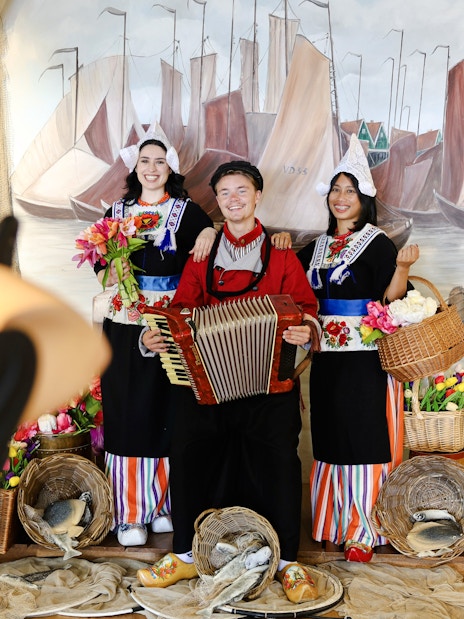 Tourists in traditional Volendam costumes posing with an accordion and baskets of flowers.
