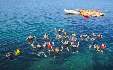 Group snorkeling in clear blue waters of Mallorca with kayaks and a boat nearby.