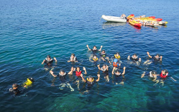 Group snorkeling in clear blue waters of Mallorca with kayaks and a boat nearby.