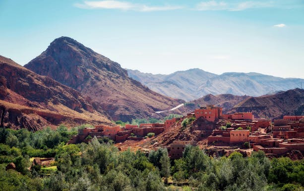 Traditional Berber village in the Atlas Mountains, Morocco, with rugged peaks in the background.