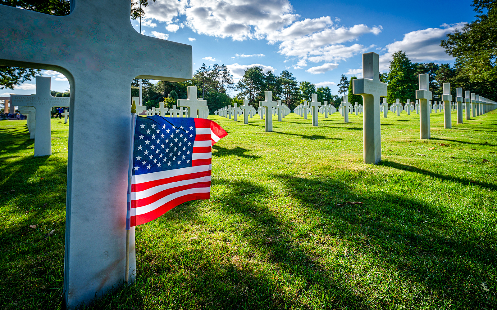 American flag beside white crosses at the American War Cemetery in Normandy, France.