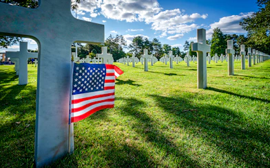 American flag beside white crosses at the American War Cemetery in Normandy, France.