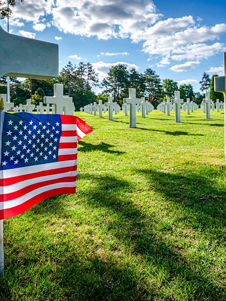 American flag beside white crosses at the American War Cemetery in Normandy, France.