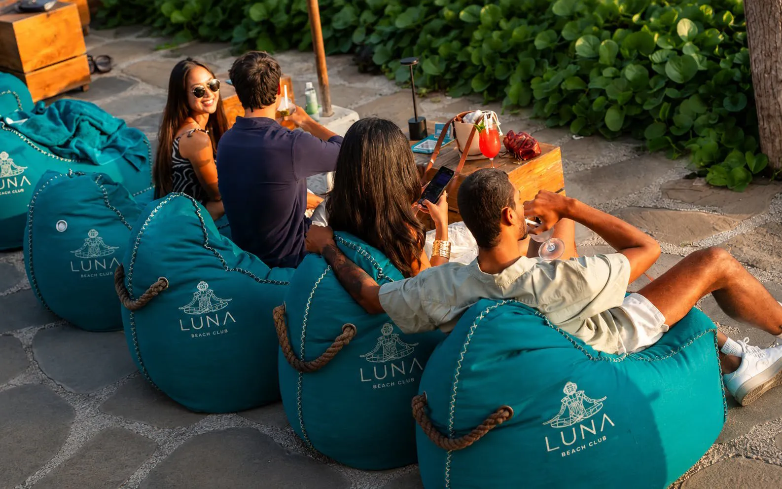 Guests relaxing on bean bags at Luna Beach Club with drinks.
