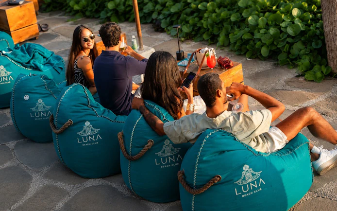 Guests relaxing on bean bags at Luna Beach Club with drinks.
