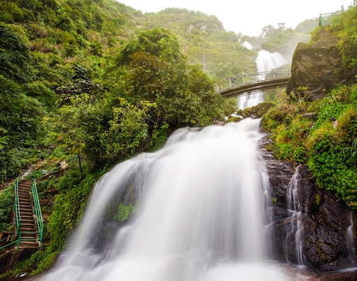Silver Waterfall cascading through lush greenery in Sapa, Vietnam, with a bridge above.
