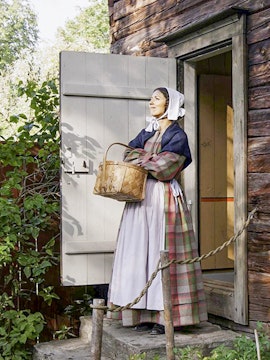 Woman in traditional attire holding a basket at Skansen Open Air Museum, Sweden.