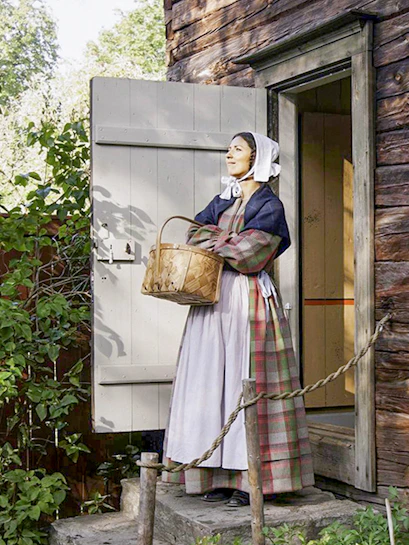 Woman in traditional attire holding a basket at Skansen Open Air Museum, Sweden.