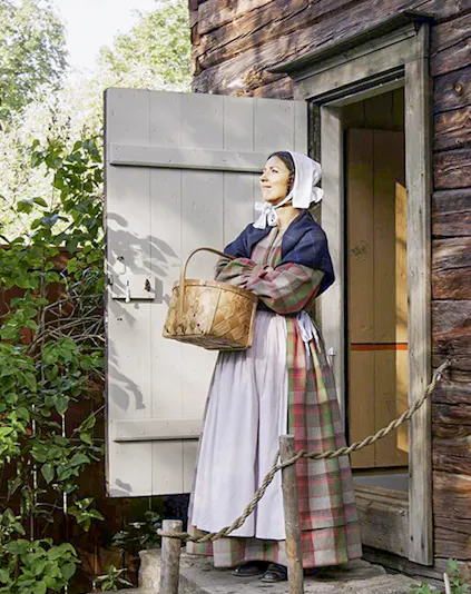 Woman in traditional attire holding a basket at Skansen Open Air Museum, Sweden.