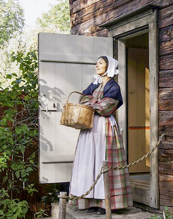 Woman in traditional attire holding a basket at Skansen Open Air Museum, Sweden.