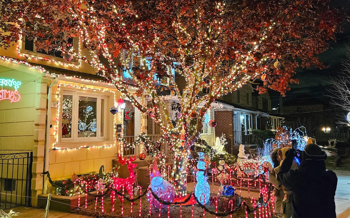 Christmas lights display on a New York house with festive decorations and visitors taking photos.