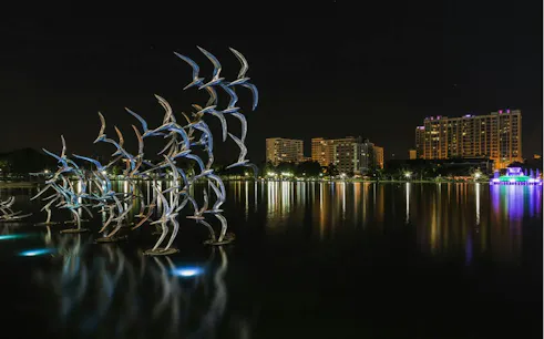 Night view of Lake Eola with illuminated bird sculpture and city skyline, Orlando.