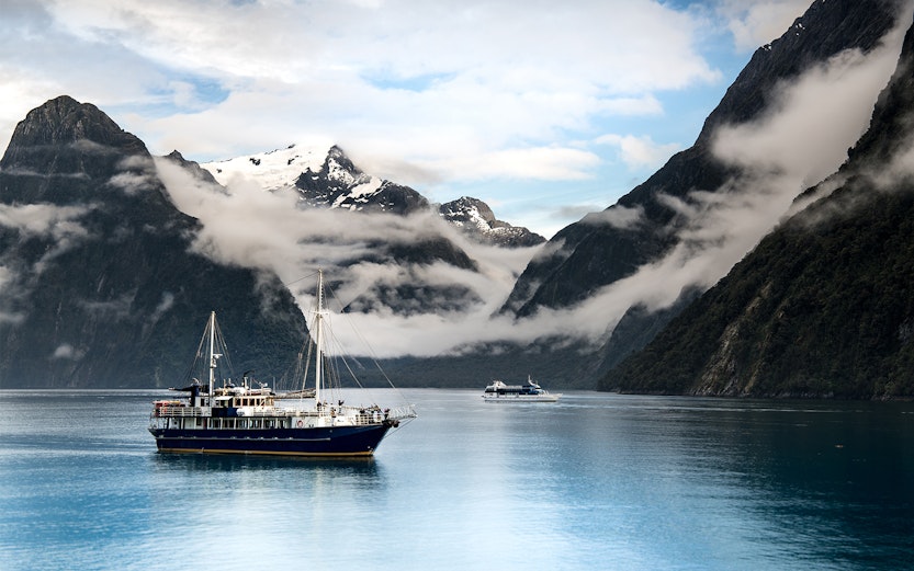Cruise ship sailing through Milford Sound with misty mountains in the background.