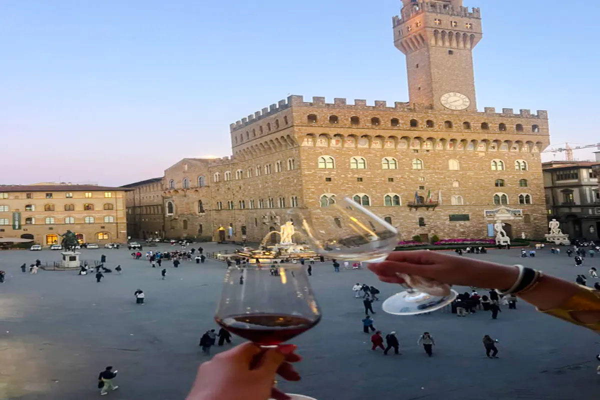 Toasting wine glasses overlooking Piazza della Signoria, Florence at dusk.