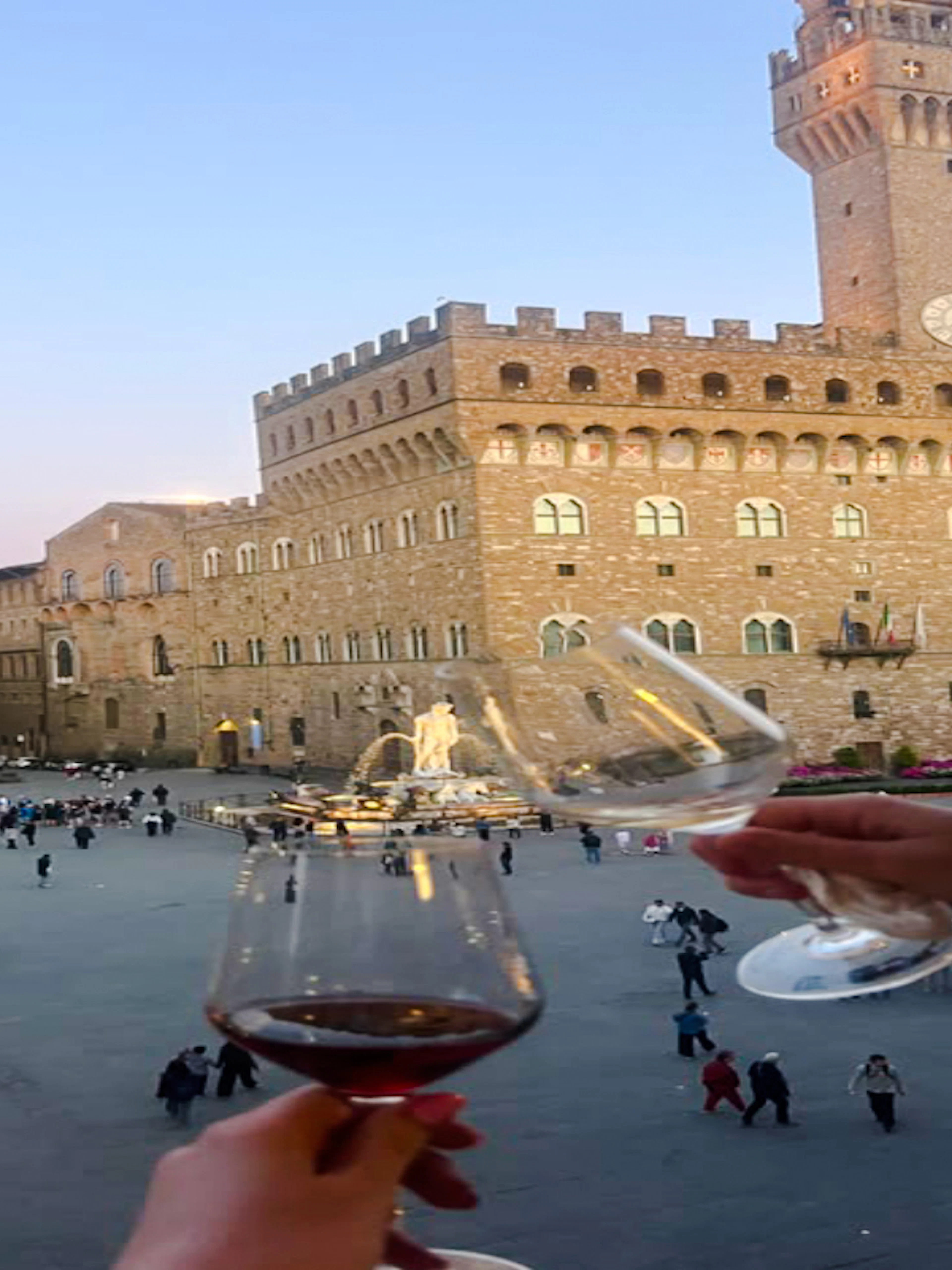 Toasting wine glasses overlooking Piazza della Signoria, Florence at dusk.