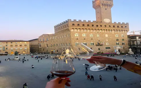 Toasting wine glasses overlooking Piazza della Signoria, Florence at dusk.