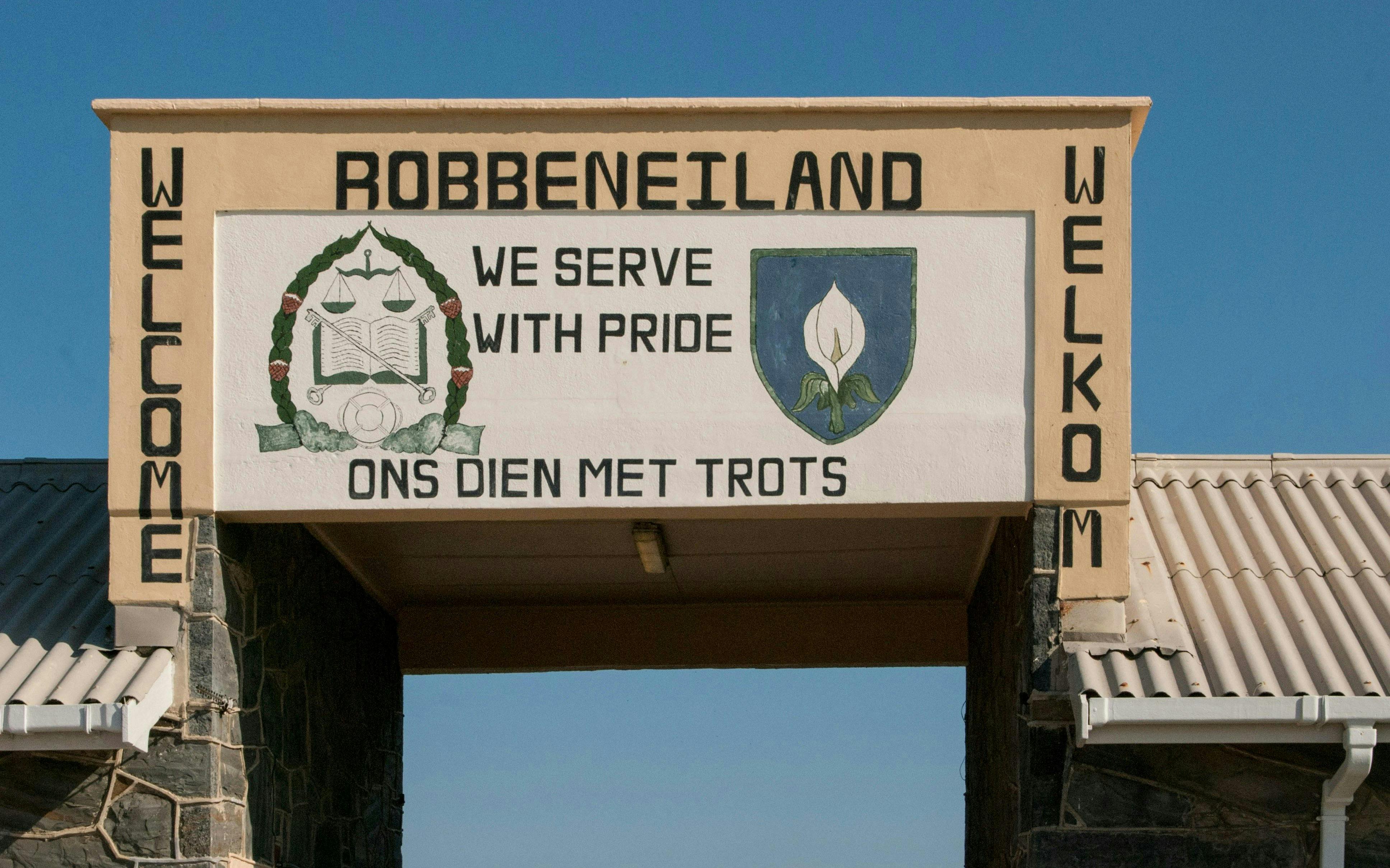 Entrance sign at Robben Island Prison with emblem and motto in English and Afrikaans.