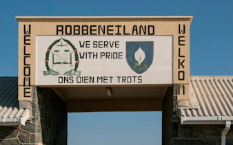 Entrance sign at Robben Island Prison with emblem and motto in English and Afrikaans.