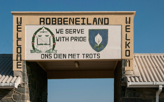 Entrance sign at Robben Island Prison with emblem and motto in English and Afrikaans.