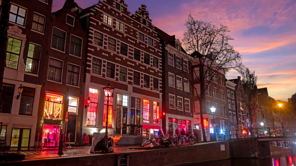 Amsterdam Red Light District canal at dusk with illuminated buildings and bicycles.