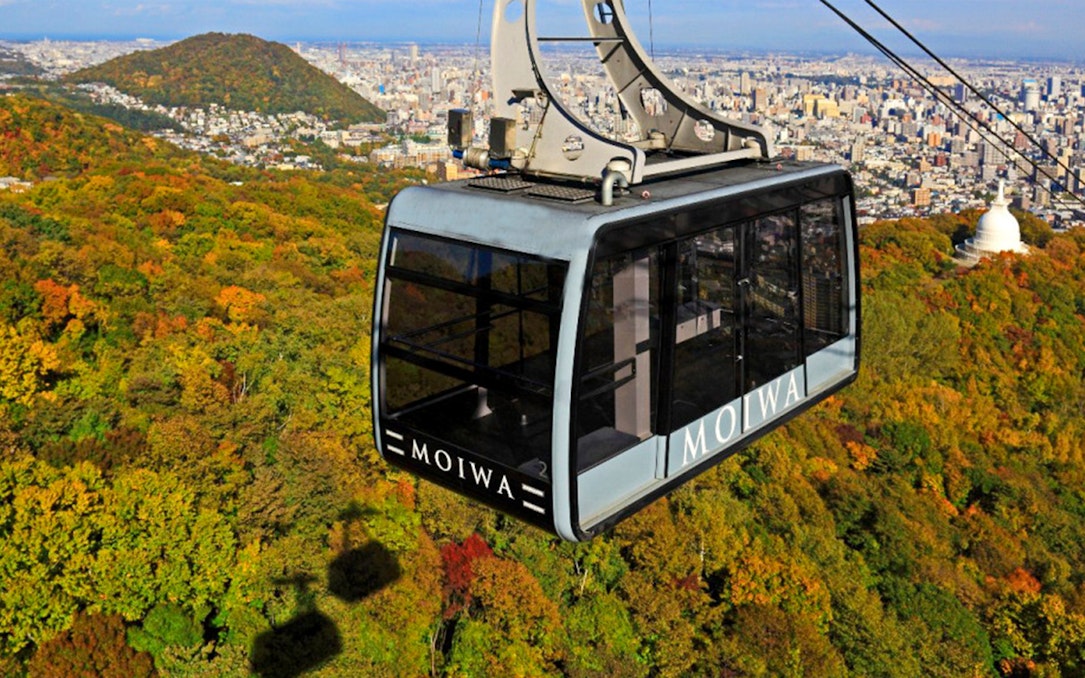 Mt. Moiwa ropeway car over autumn forest with Sapporo cityscape in background.