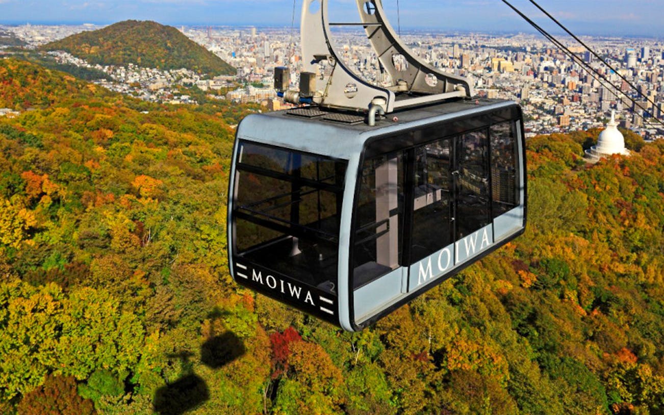 Mt. Moiwa ropeway car over autumn forest with Sapporo cityscape in background.