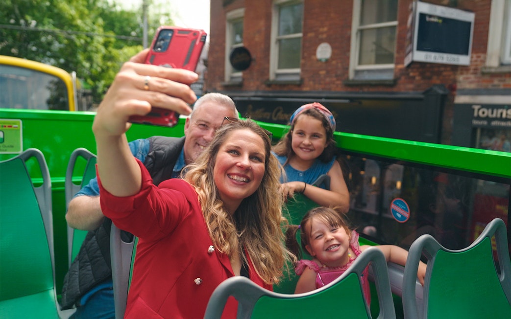 Family taking a selfie on a hop-on hop-off bus tour in the city.
