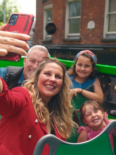 Family taking a selfie on a hop-on hop-off bus tour in the city.