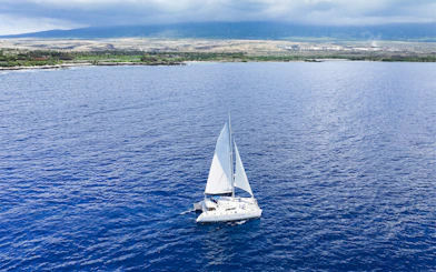 Catamaran sailing on blue waters near Kona, Hawaii with coastline in the background.